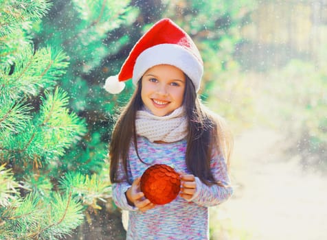 Christmas smiling child little girl in santa red hat with ball near tree 