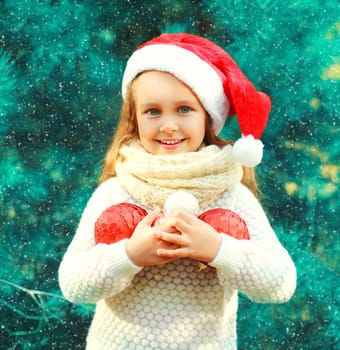 Christmas smiling child little girl in santa red hat with many balls near a tree