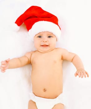Christmas, family concept - cute baby in red santa hat lying on white bed at home