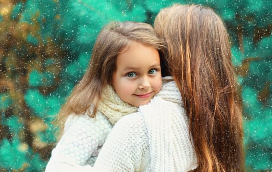 Happy little girl child hugging her mother in winter day over tree