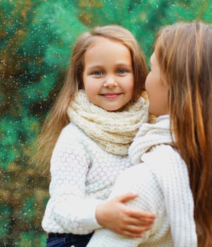 Happy little girl child hugging mother in winter day over tree