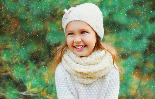 Smiling little girl child wearing a knitted hat and sweater with scarf near christmas tree