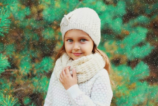 Little girl child wearing knitted hat and sweater with scarf near christmas tree