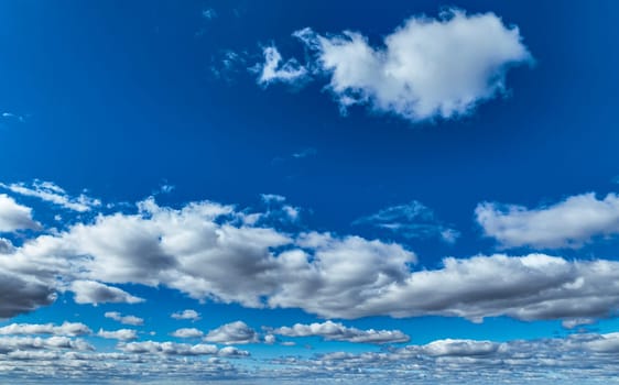 A brilliant expanse of blue sky dotted with fluffy white clouds creates a serene atmosphere during the afternoon. The light shines through the clouds, enhancing the scene's beauty.