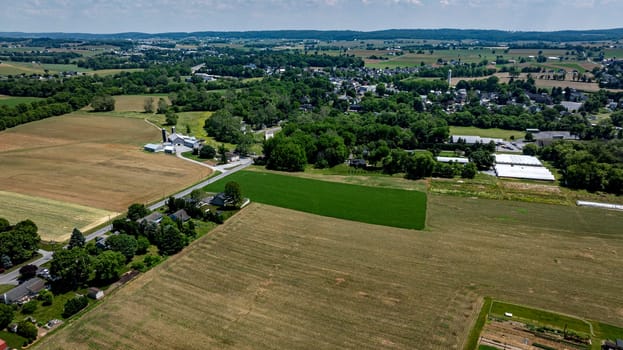 The landscape showcases a vibrant patchwork of green fields and brown farmland stretching toward a small town under a clear blue sky, typical of Pennsylvania's rural charm.