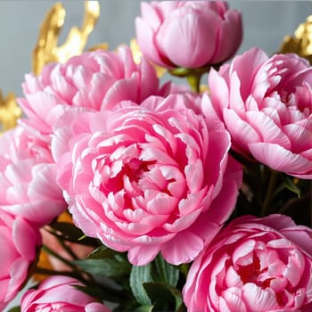 This arrangement features lush pink peonies surrounded by golden foliage, creating a striking and elegant tableau perfect for home decor or special occasions.