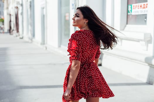 Beautiful woman in a red summer dress walking through the streets of the city