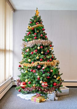 Tall Christmas tree decorated with balls, lights, and glittering firs installed in the corner of a room