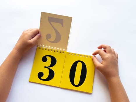 Childs hands flip through yellow pages with numbers on a white background.