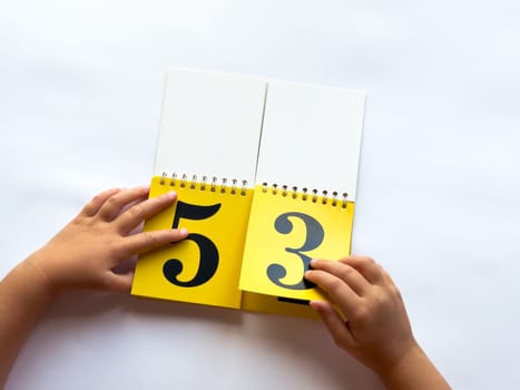 Child flipping yellow calendar pages with numbers on white background.