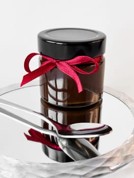 Elegant glass jar with red ribbon on mirrored surface.