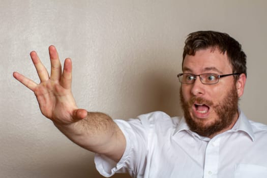 A bearded man wearing glasses and a white shirt expresses surprise while reaching out with his hand. The moment captures curiosity and unexpected reaction.