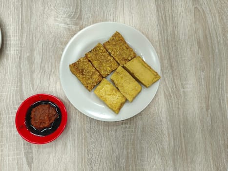 A plate of fried tempeh and tofu, a popular Indonesian dish. Served on a white plate with traditional chili paste.