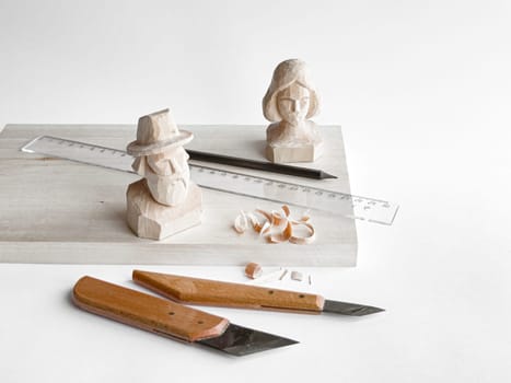 Wood carving tools with handcrafted busts on display board.