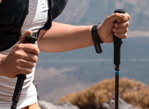 Man doing sports, traveling and hiking, holding trekking poles in his hands and climbing mountain slope, walking with poles on rocky trail outdoors, close-up view.