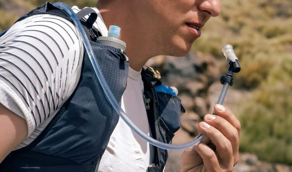 Man drinks water from drinking system, hydration pack in backpack during jogging and hiking in the mountains, athlete trains, leads active lifestyle, involved in trail running.