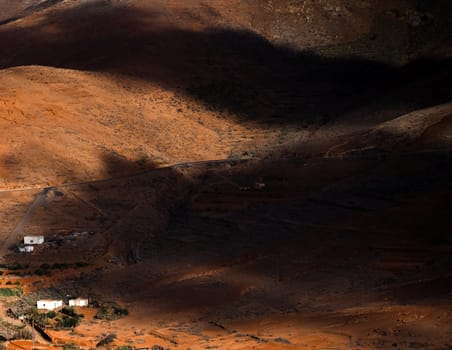 Landscape of Fuerteventura island with red soil, reddish tint of valleys and mountains and white houses of small villages. Aerial photo view from above on the area with beautiful shadows from clouds.