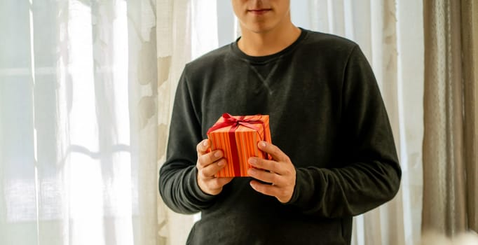 Young man in a casual gray sweater holds a bright beautifully wrapped gift in his hands, a surprise for a loved one for a birthday or another celebration, like Christmas, Valentine's Day, Anniversary.