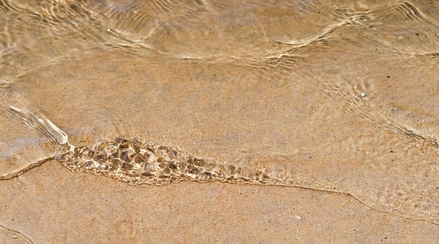 Clear calm and clean water close-up, the ocean washes the coast with a sandy beach on a sunny day.