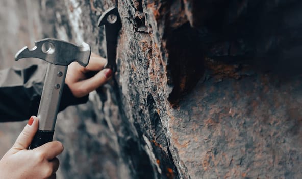Women's hands hold a climbing hammer and drive the anchor into the rock, the climber makes a belay point on the route to the top of the mountain.