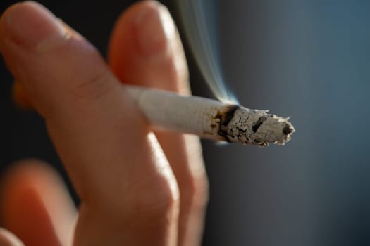 Cigarette with ashes and smoke close-up, macro. Concept about tobacco, nicotine and harm to health.