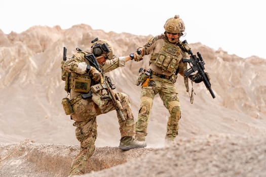 One soilder or military man pull his friend up from slope in area near the mountain during outdoor practice.