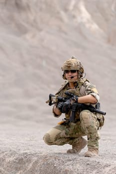 One military or soldier with gun sit in battlefield near the mountain and look forward during outdoor practice.