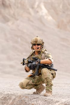 Vertical image of military or soldier with gun sit in battlefield near the mountain and look at camera during outdoor practice.