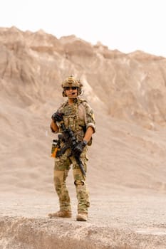 Vertical image of military or soldier with gun stand in battlefield near the mountain and look to camera during outdoor practice.