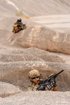 Vertical image military or soilder man hold gun and sit in the pit or slope in front of the terrorist who stay in back of battlefield in area near mountain.