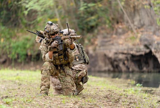 Two militaries or soldiers stay in battlefield near the river with sit down and point gun in different direction during outdoor practice.