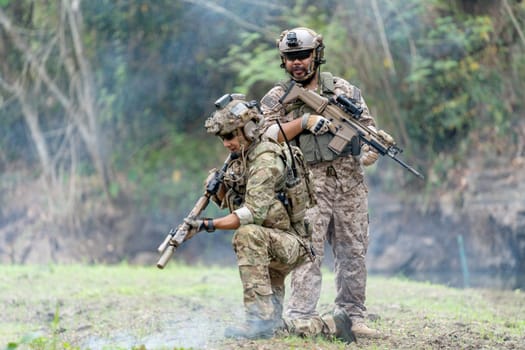 Two militaries or soldiers stay in battlefield near the river with one sit down and one stand in the back  during outdoor practice.
