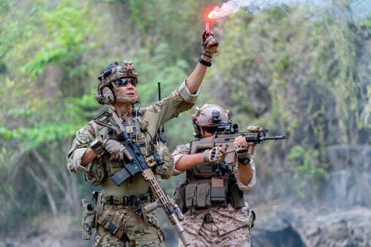 Close up two militaries or soldiers stay in battlefield near the river with one hold flare fireworks and one stand with point gun forward direction during outdoor practice.