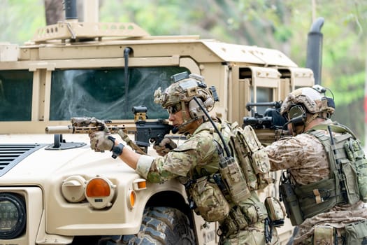 Wide shot of two militaries or soldiers stay in front of humvee car area of car hood and point gun to left side during outdoor practice.