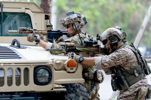 Two militaries or soldiers stay in front of humvee car area of car hood and point gun to left side during outdoor practice.