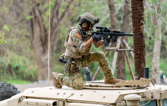 Military or soldier stay on car roof and point gun to right side during outdoor practice.