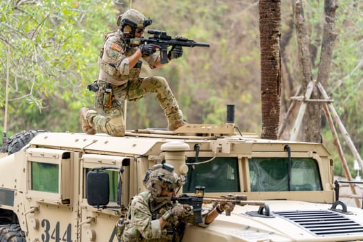 Two militaries or soldiers stay near humvee car with on on roof and the other one in area of car hood also point gun to right side during outdoor practice.