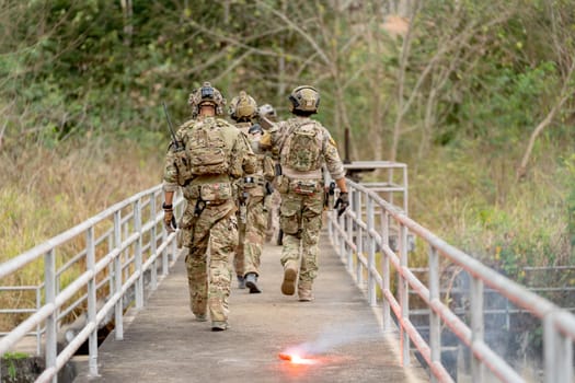 Back of military or soldier team with battle suit walk on the bridge near flare firework during outdoor practice.