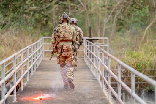 Back of military or soldier team with battle suit walk on the bridge near flare firework during outdoor practice.