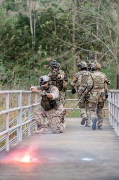 Vertical image of military or soldier team with battle suit stay on the bridge near flare firework in position for battle and point gun different direction during outdoor practice.