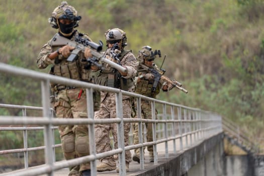 Side view group of military or soldier team with battle suit stand on the bridge and point gun down direction to enemy during outdoor practice.