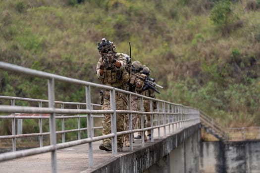 Front view of group of militaries or soldiers with battle suit hold and point gun and walk in the row on bridge during outdoor practice.