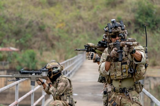 Close up military or soldier team with battle suit stand on the bridge and point gun to enemy in different direction during outdoor practice.