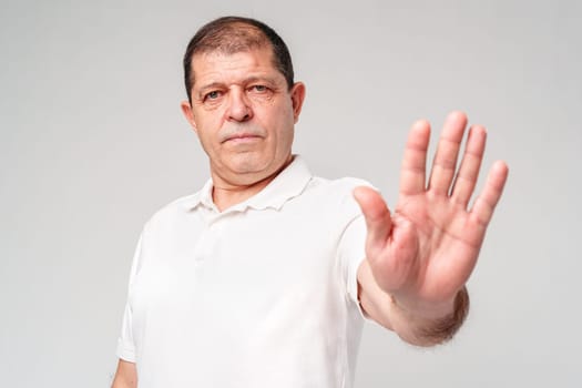 A middle-aged man wearing a white polo shirt holds up his hand while looking directly at the camera