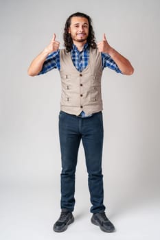Young man with curly hair gives a thumbs-up in a casual outfit against a neutral background close up