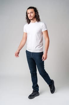 A young man with curly hair stands confidently against a neutral background in studio