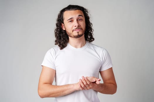 A young man stands thoughtfully against a plain background, expressing contemplation close up