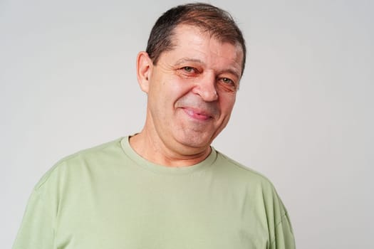Friendly older man smiling warmly in a light green shirt against a neutral background close up