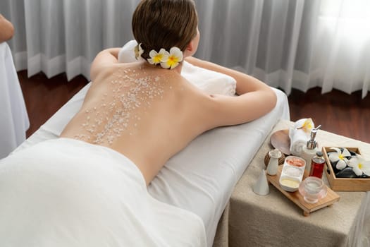 Woman customer having exfoliation treatment in luxury spa salon with warmth candle light ambient. Salt scrub beauty treatment in health spa body scrub. Quiescent