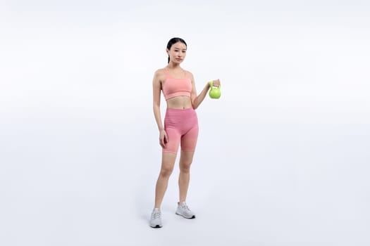 Vigorous energetic woman doing kettlebell weight lifting exercise on isolated background. Young athletic asian woman strength and endurance training session as body workout routine.